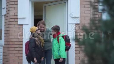 一位年轻的高加索女人抱着她的孩子送他们上学。 带背包的兄妹